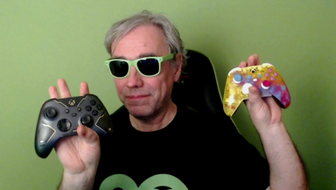 maguzzolo smiles in a t-shirt with the Xbox 20 year anniversary logo on it, holding two custom controllers up in his hands. He's wearing green sunglasses. 